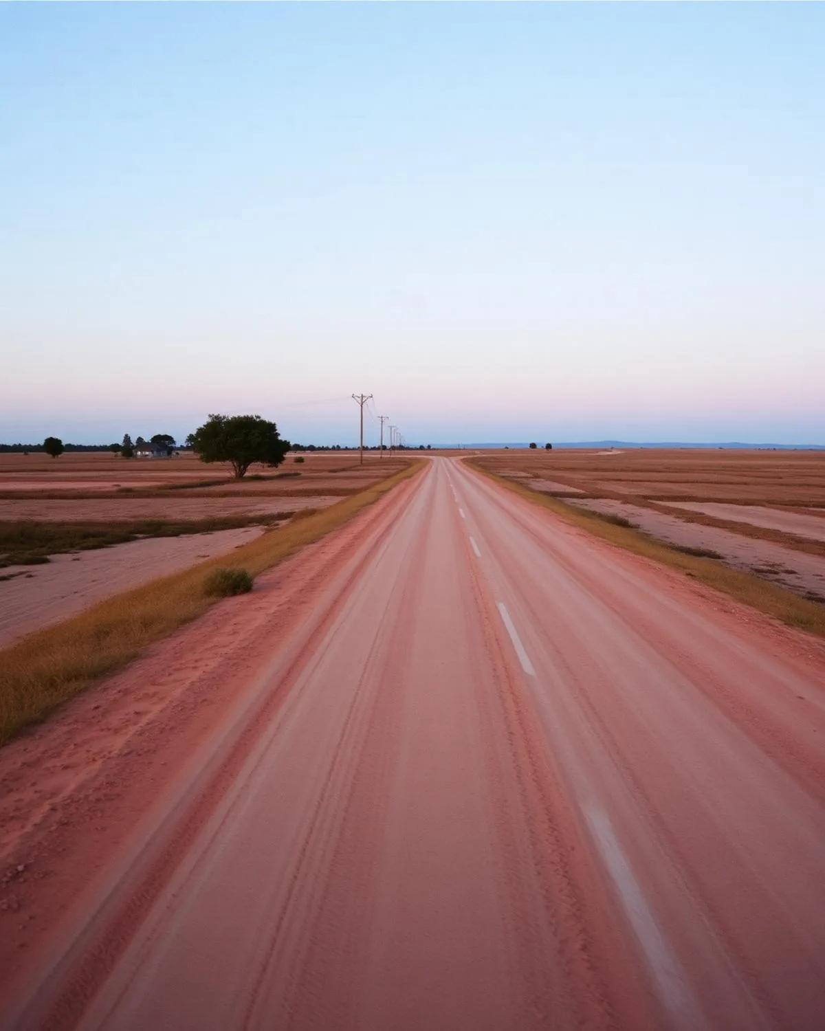 Estrada de terra vermelha atravessando o sertão em direção ao horizonte, céu amplo em tons azul e areia ao amanhecer.